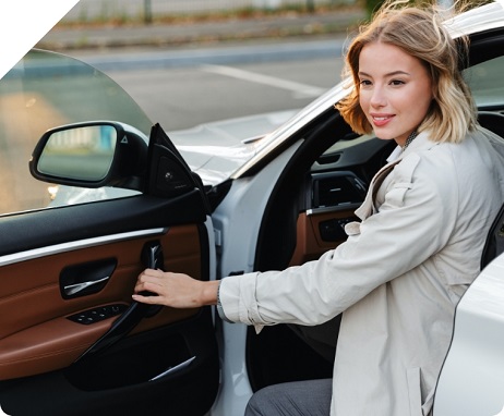 Woman exits her car with her hand on the door handle. 